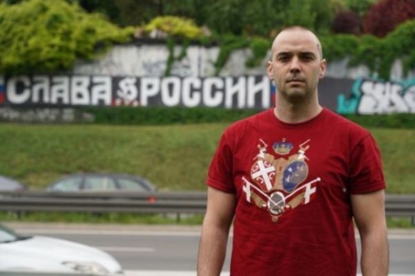 Damjan Knezevic stands in front of street graffiti in Belgrade which reads 'Glory to Russia' in Russian
