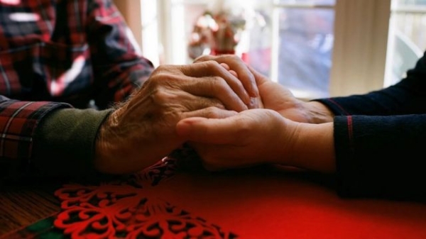 An elderly man and younger woman holding hands