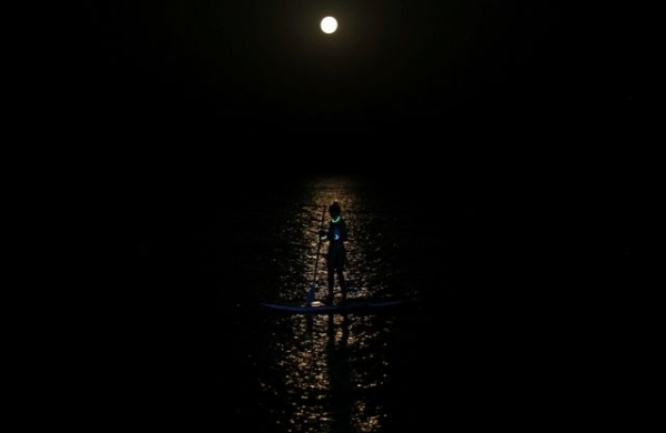 A person paddles on a board while a full moon illuminates the water in Larnaca, Cyprus