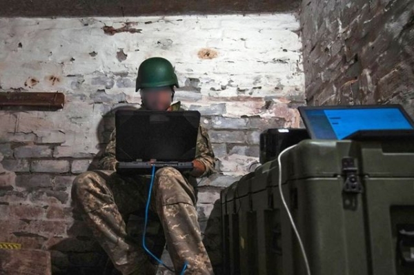 Ukrainian soldier leans over his laptop in a damp basement