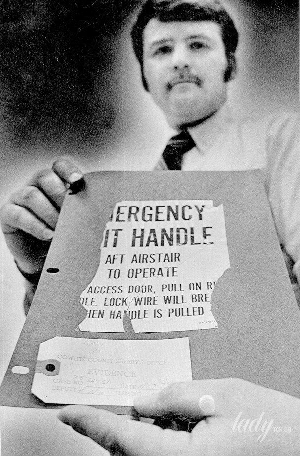 Detective Bob Nix demonstrates a placard with instructions for exiting a Boeing 727, found by a hunter near the town of Toutle and missing with D. B. Cooper / © Associated Press